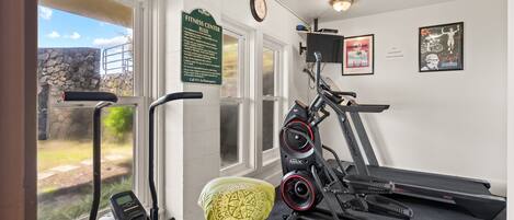 A gym with cardio equipment, a wall-mounted clock, and a sign with fitness rules.