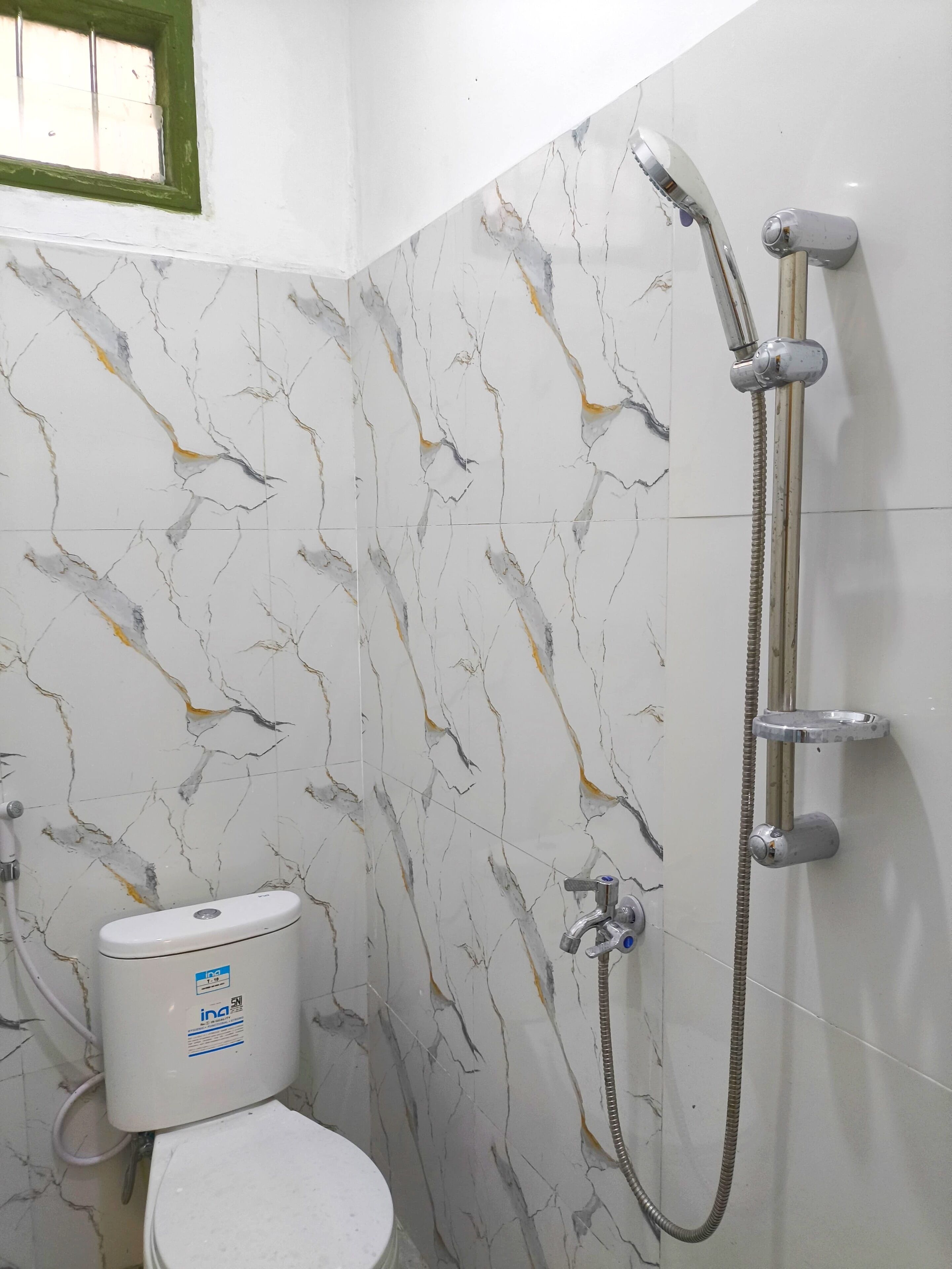 A bathroom with a toilet, a shower, and a marble-patterned wall.