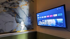 A flat-screen TV mounted on a wall displaying the Marvel Studios Avengers movie poster.