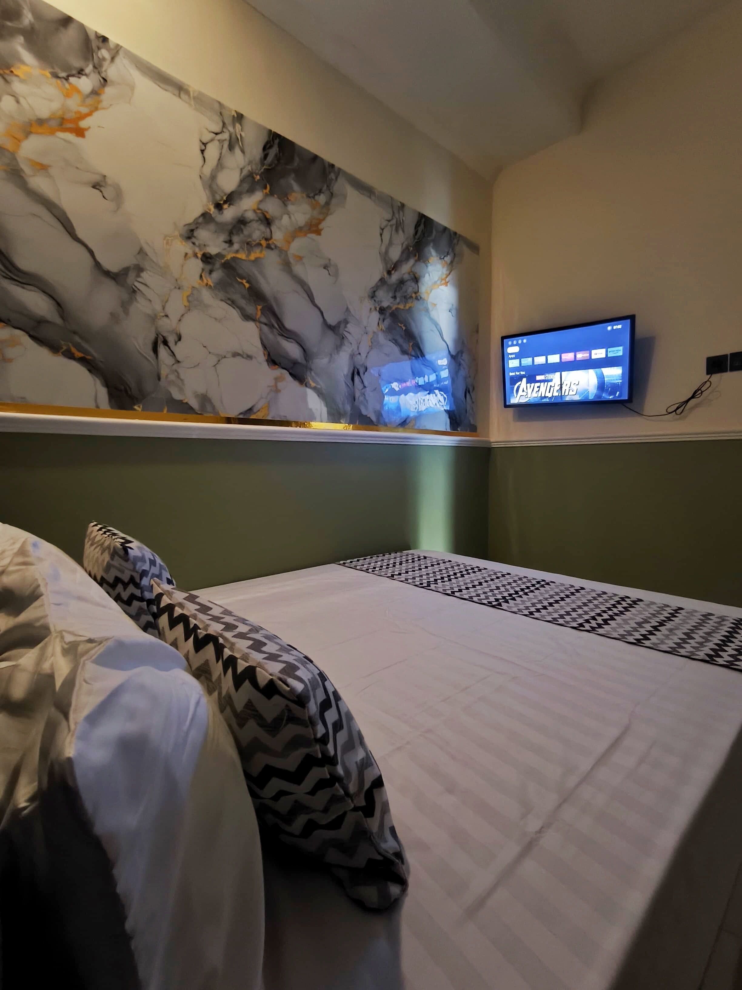 A hotel room with a bed, a television mounted on the wall, and a marble artwork above the bed.