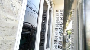 A narrow corridor with a tiled floor, a window with a metal grille, and a wall with a marble-like pattern.
