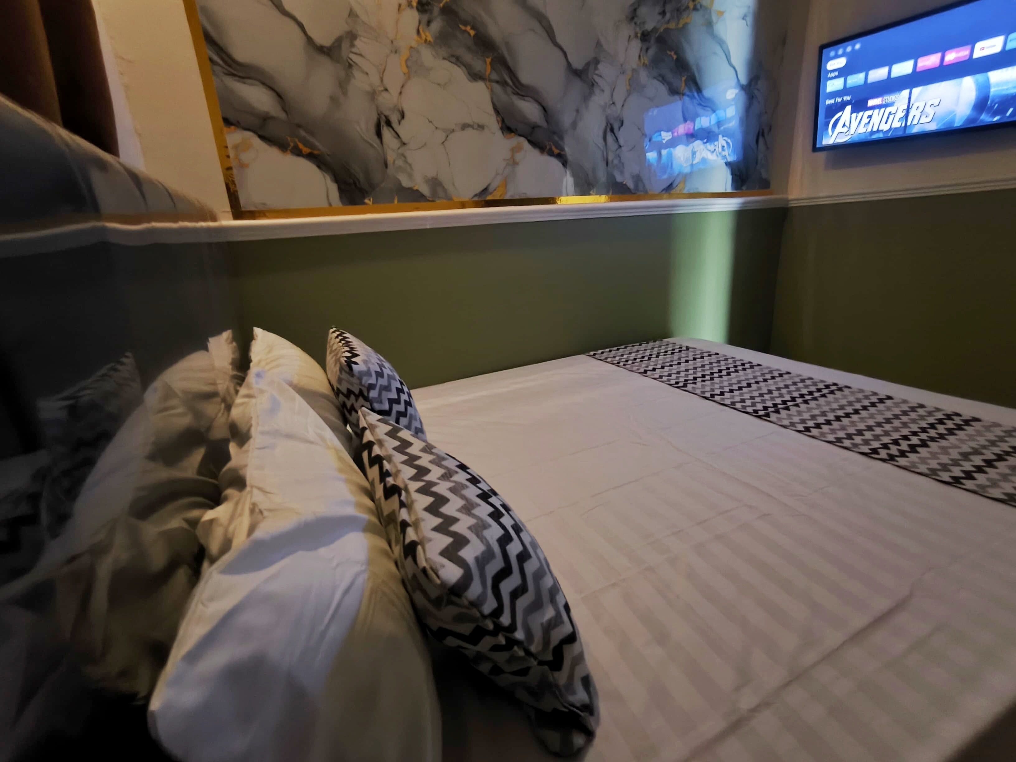 A hotel room with a bed, pillows, a TV displaying 'Avengers: Endgame', and a marble wall.