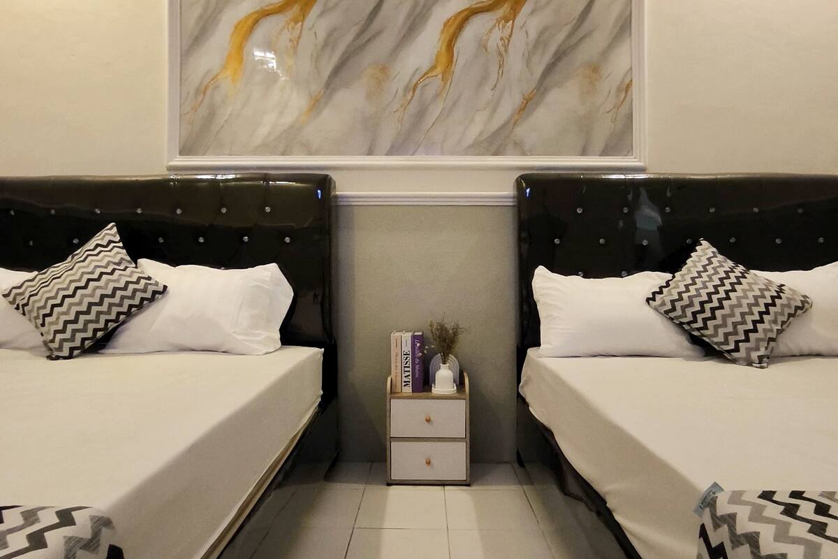 Una camera da letto moderna con due letti, un comodino con libri e un vaso, e un’opera d’arte in marmo a parete.