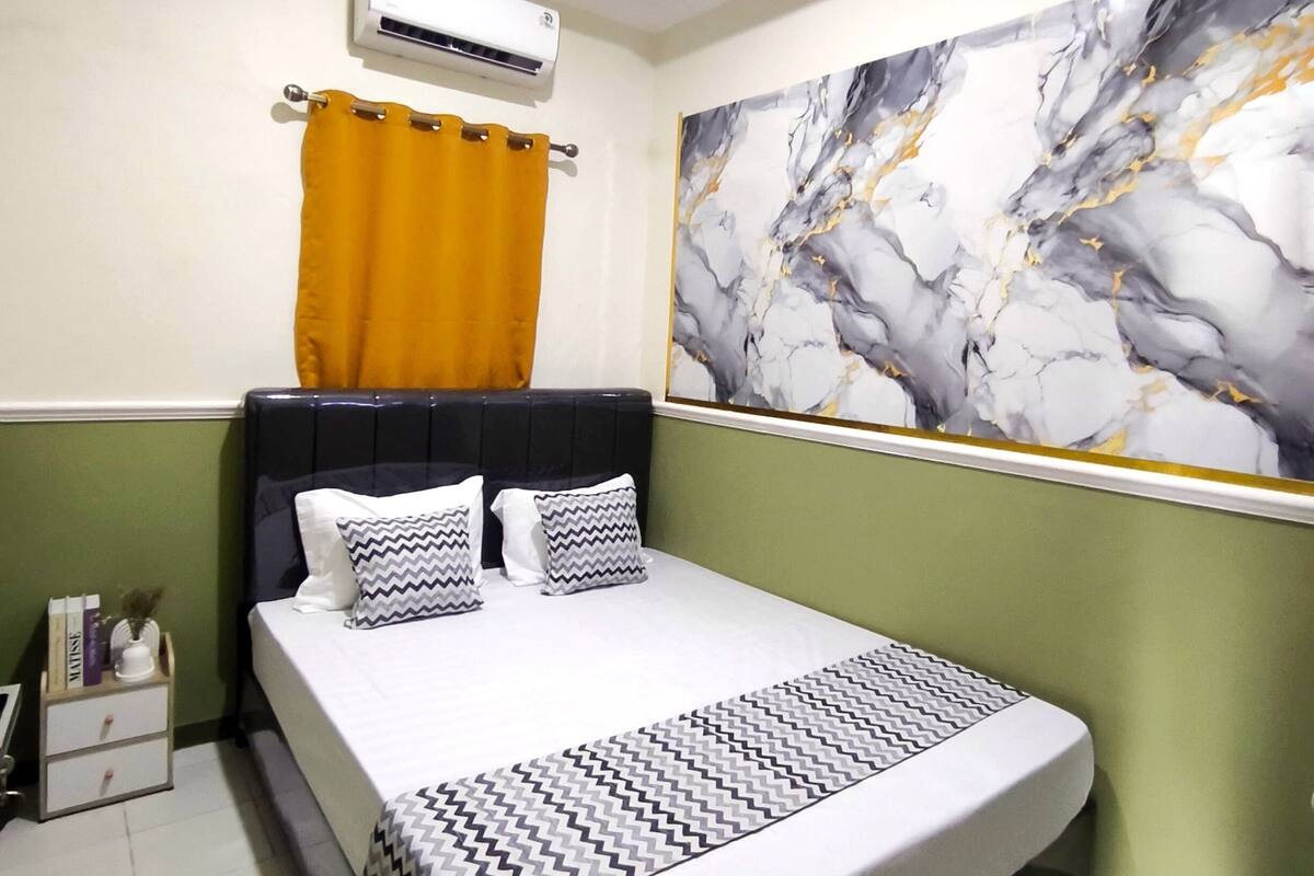 Una camera da letto ordinata con un letto, un comodino, un condizionatore d'aria a parete e un grande quadro astratto.