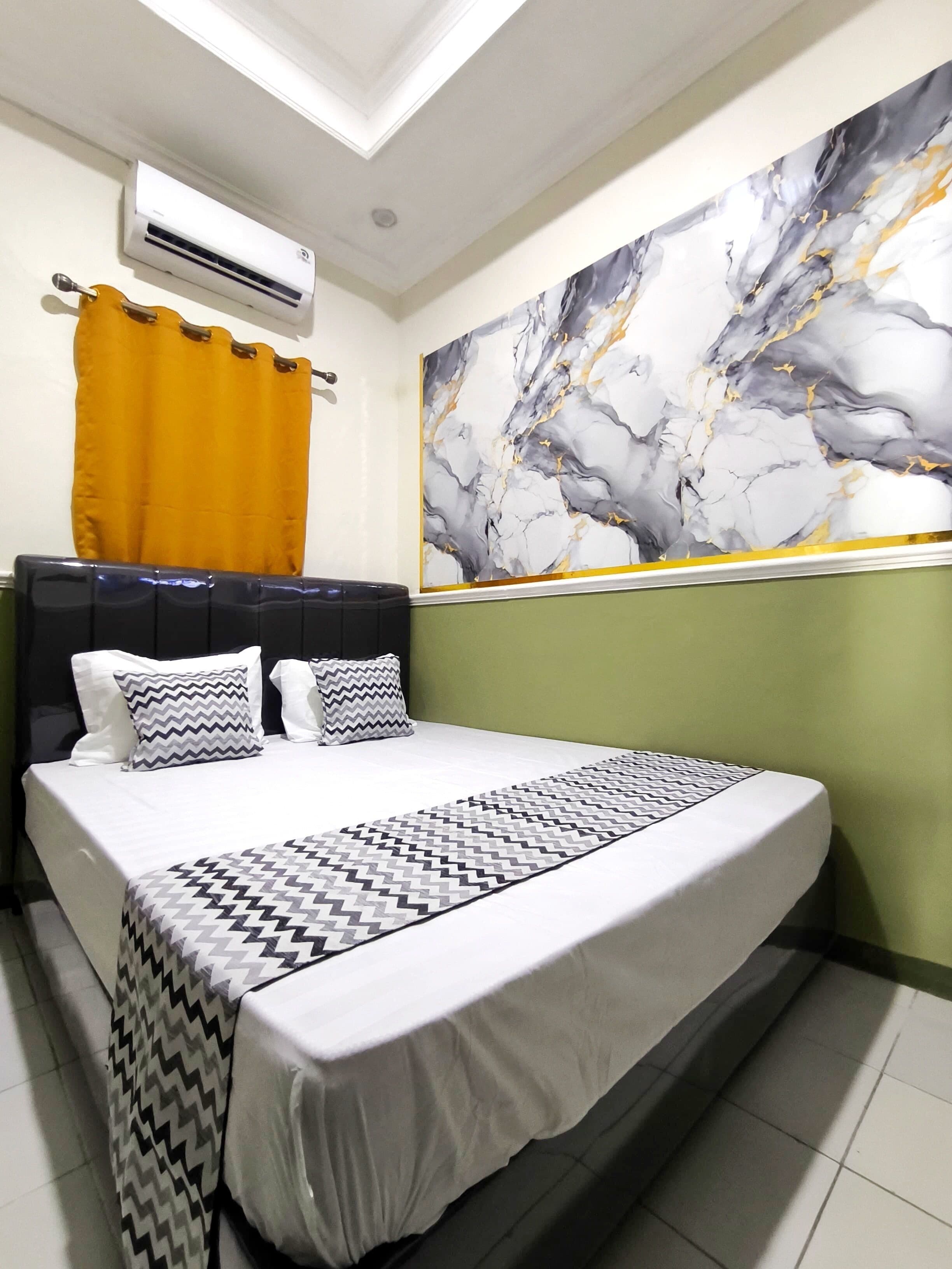 Camera da letto con un grande letto, una testiera, un condizionatore d'aria a parete, una tenda e un quadro decorativo con motivo marmorizzato.