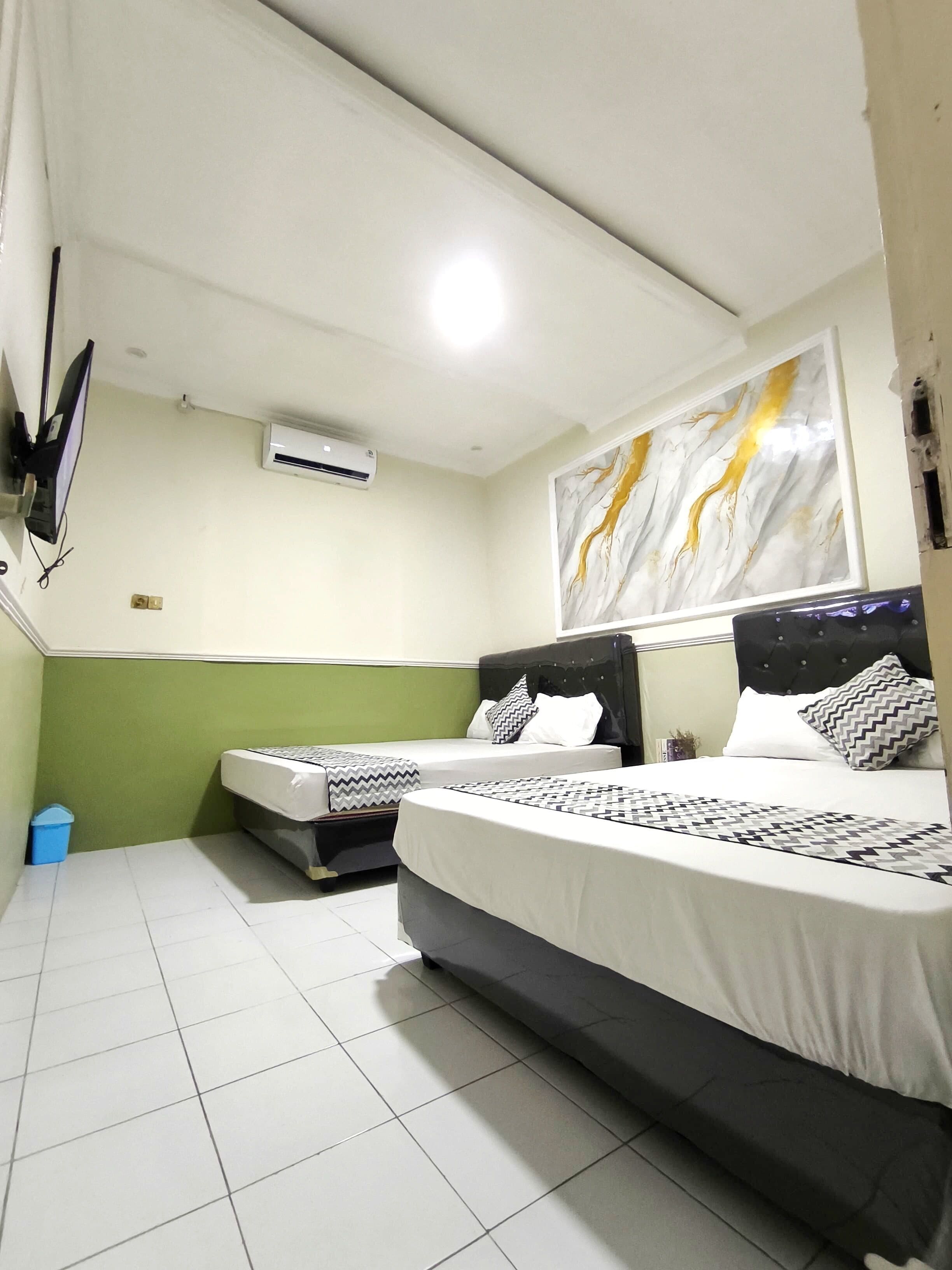 Une chambre d’hôtel avec deux lits, un téléviseur à écran plat fixé au mur, un appareil de climatisation et un élément décoratif mural.