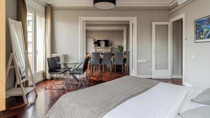 Una habitación de hotel con una cama grande, una zona de comedor con sillas y una cocina al fondo.