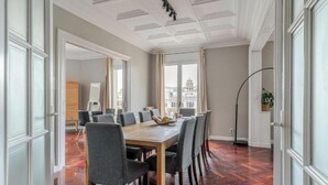 Comedor con mesa de madera, sillas grises, ventanas amplias con cortinas y vista a la ciudad.