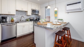 A modern kitchen with white cabinets, a granite countertop, a built-in microwave, and a large island with bar stools. - Kona Mansions E333 1 Bedroom Condo (Kailua-Kona)