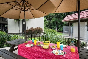 A picnic table set up outdoors with a red tablecloth, surrounded by greenery and a fenced area. - Kona Mansions E333 1 Bedroom Condo (Kailua-Kona)