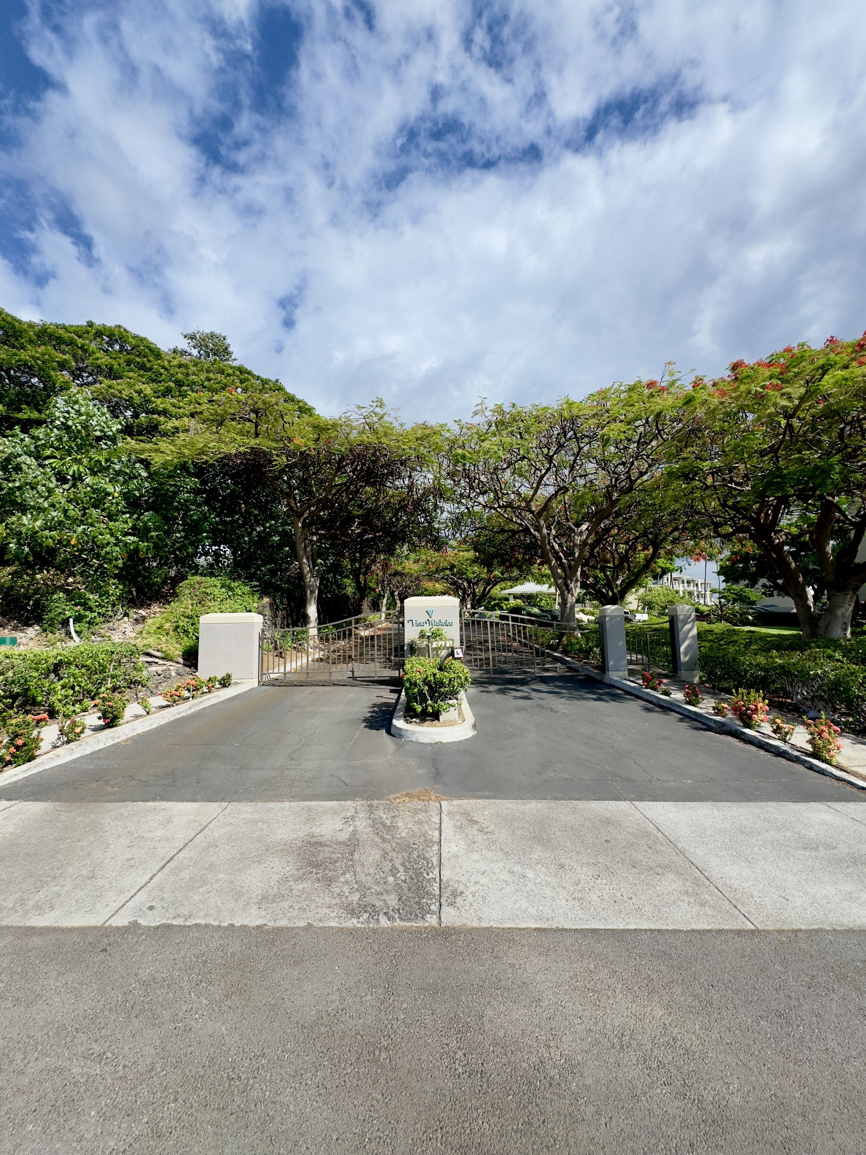 A parking area with a gated entrance, surrounded by lush greenery and trees.