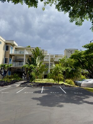 A parking lot with marked spaces, a building with multiple balconies, and surrounding greenery. - Vista Waikoloa B202 2 Bedroom Condo (Waikoloa)