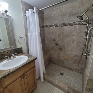 A bathroom with a shower, a sink, and a mirror. - Alii Villas #124 1 Bedroom Condo (Kailua-Kona)