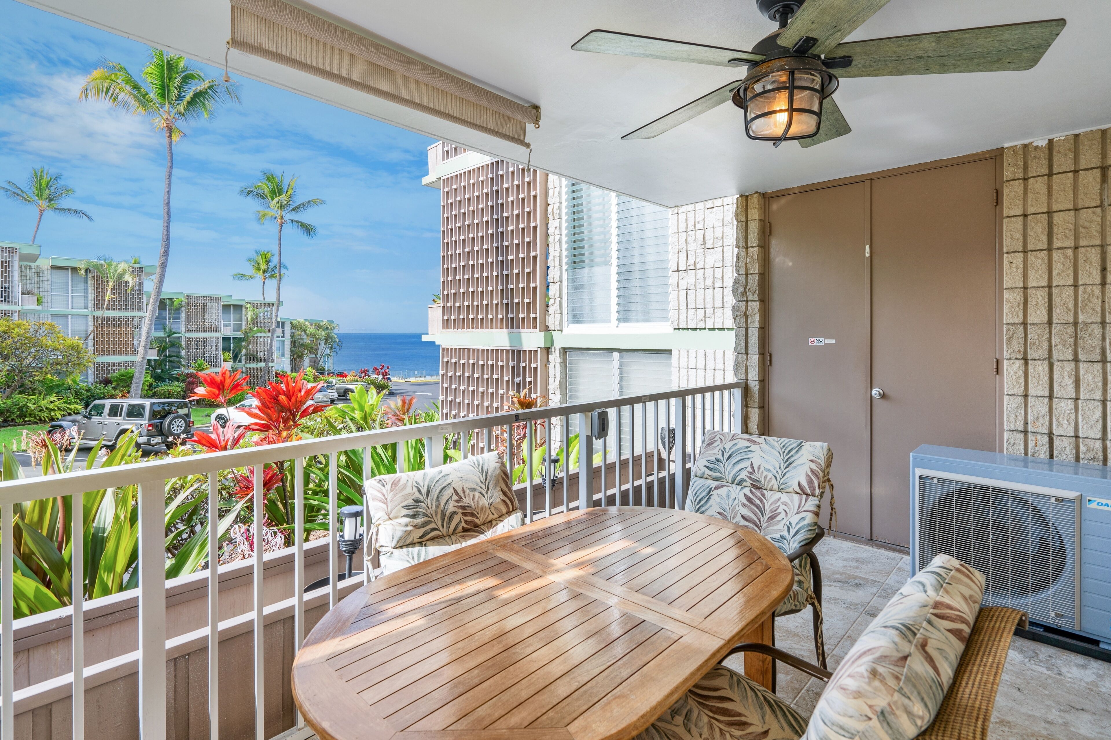 A balcony with a wooden table and chairs, a ceiling fan, and a view of the ocean and buildings.