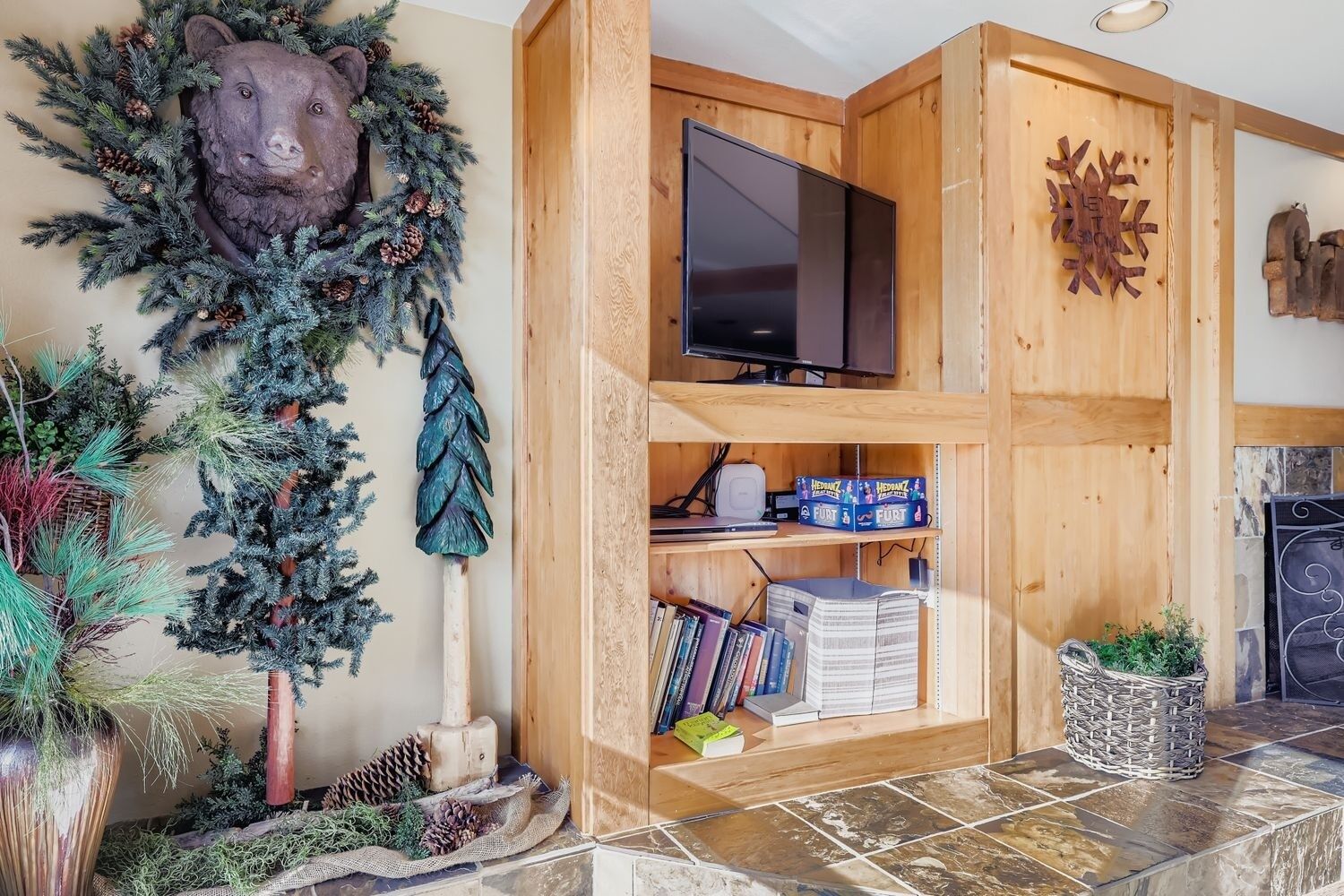 A wooden entertainment center with a flat-screen TV, shelves with books and board games, and a bear head decoration.