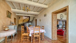 Un comedor con una mesa dispuesta para seis personas, sillas de madera, un candelabro y una escalera que lleva a otra habitación.