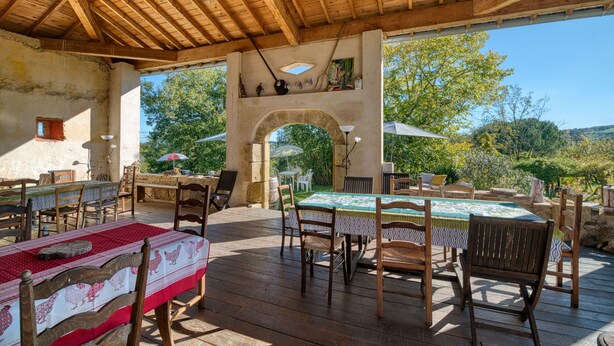 Un patio al aire libre con mesas y sillas de madera, un arco de piedra y sombrillas.