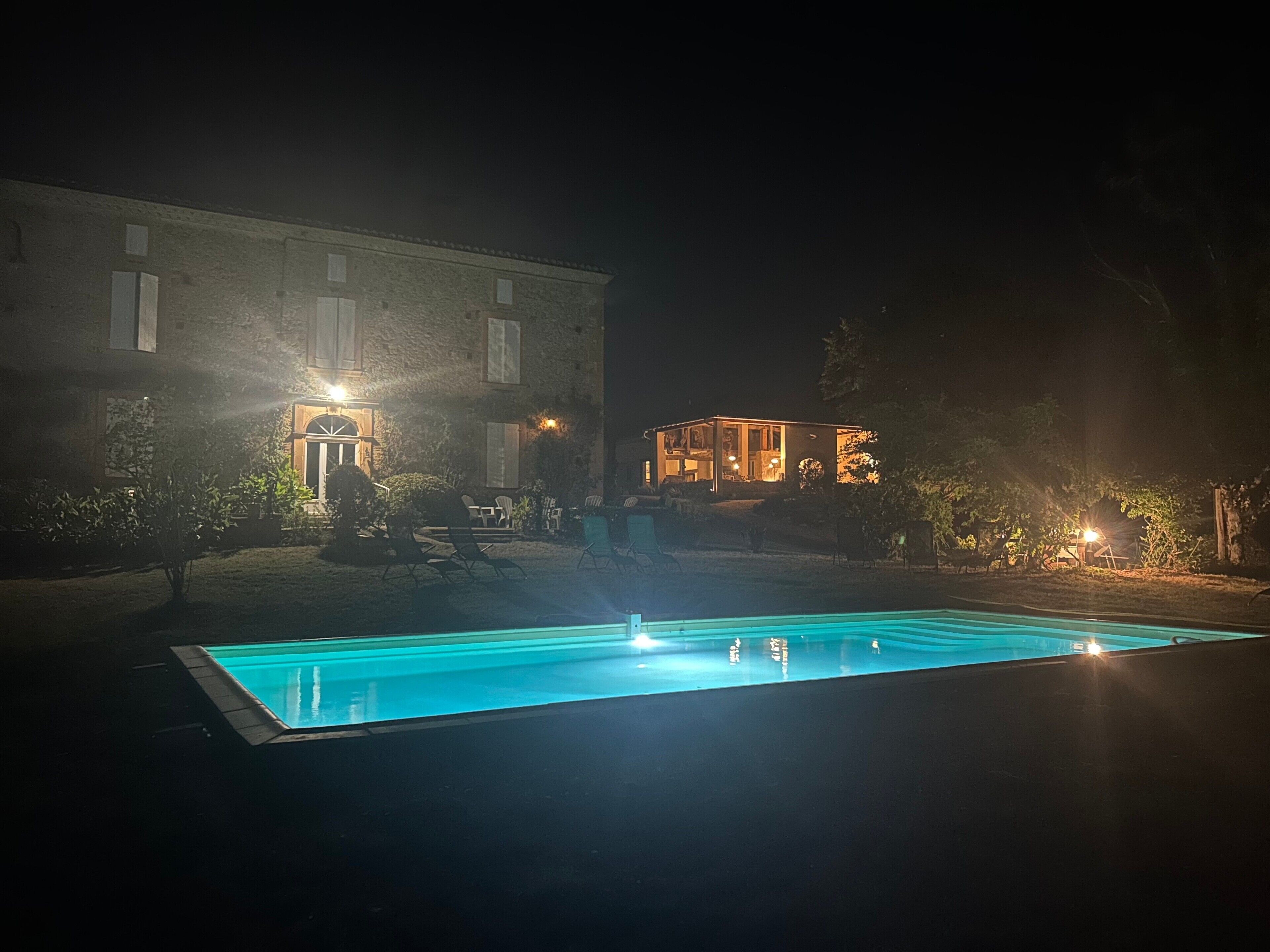 Une vue nocturne d’un bâtiment doté d’une piscine, d’un espace extérieur aménagé et de fenêtres illuminées.