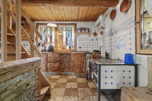Une cuisine rustique avec des poutres en bois, un mur en pierre et un sol à carreaux.