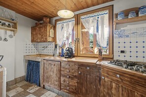 Une cuisine rustique avec des meubles en bois, une cuisinière à gaz et une fenêtre ornée de rideaux en dentelle.