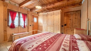 Een houten hutje met een bed, een kledingkast en een raam met gordijnen.