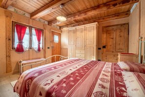 A wooden cabin with a bed, wardrobe, and a window with curtains. - Chalet 'Baita Mas Sternai Nel Parco' with Mountain View, Private Garden and Wi-Fi (Bagni di Rabbi)