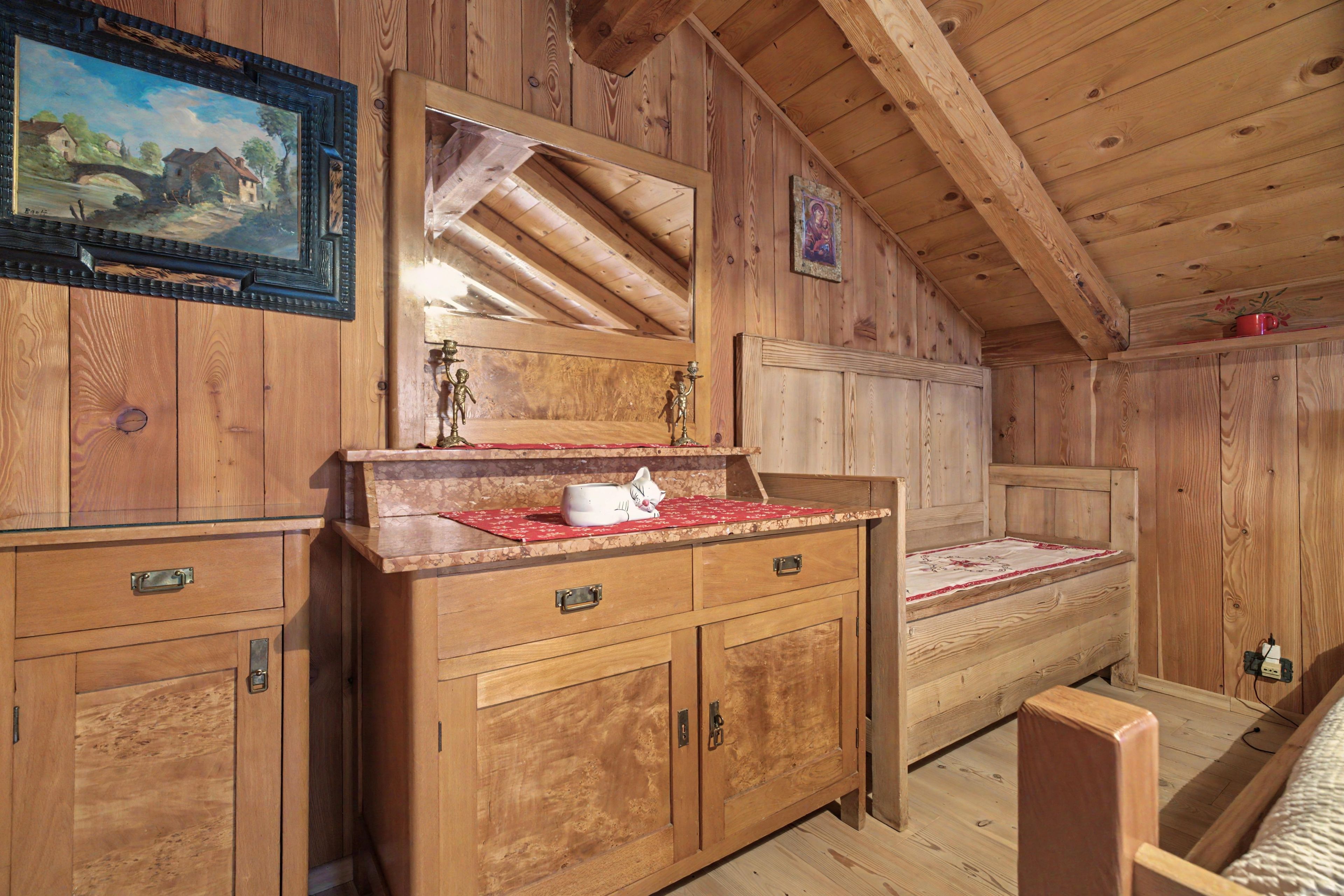 A wooden cabin interior with a bed, dresser, and a painting on the wall.