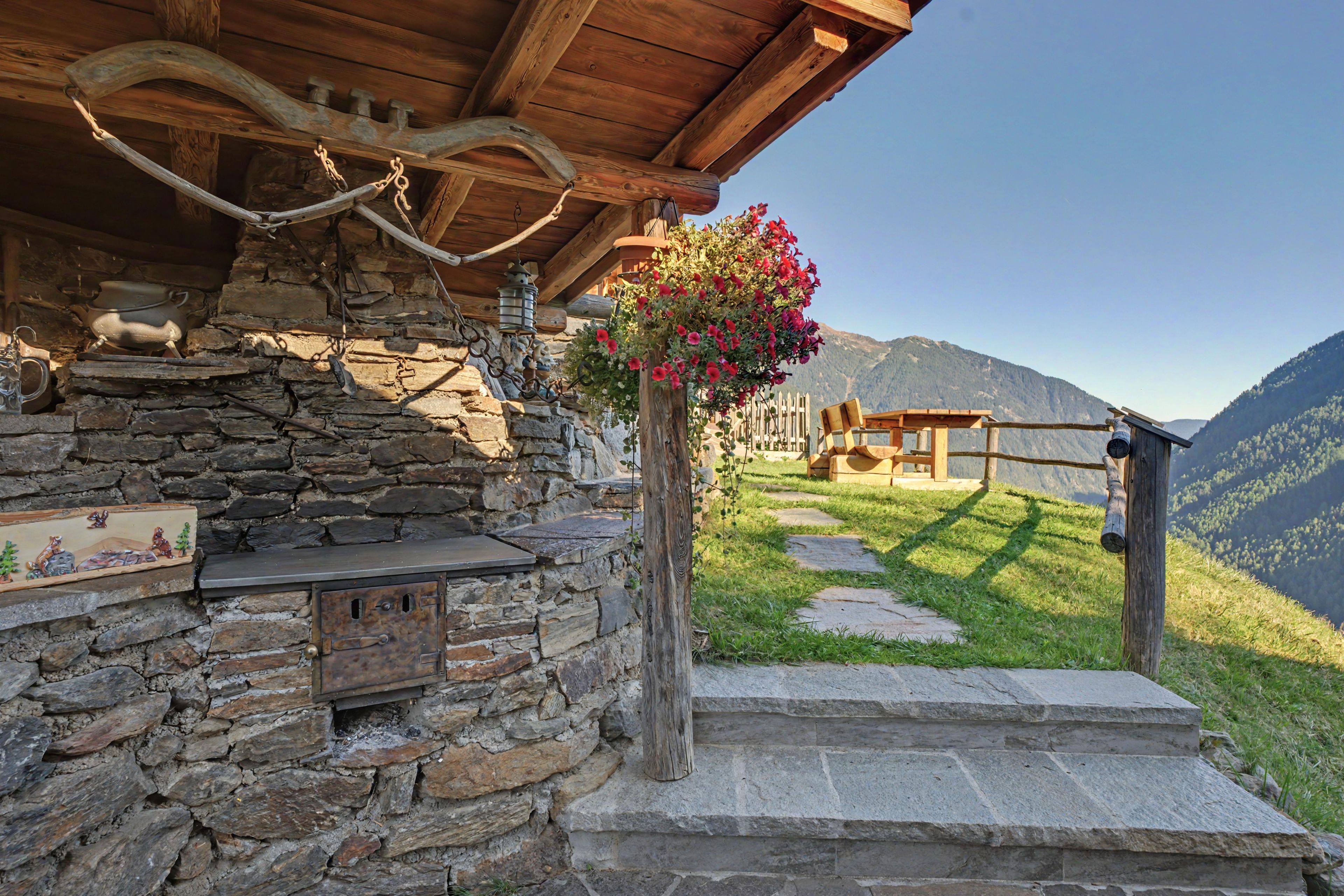 A rustic stone building with a wooden porch, stone steps, and a flower arrangement.