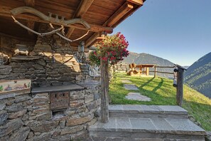 Un bâtiment rustique en pierre, doté d’un porche en bois, d’un escalier en pierre et d’une composition florale.