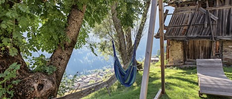 Una hamaca colgada entre árboles, una terraza de madera y una construcción rústica con techo de paja.