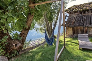 Un hamac suspendu entre des arbres, une terrasse en bois et un bâtiment rustique avec un toit de chaume.