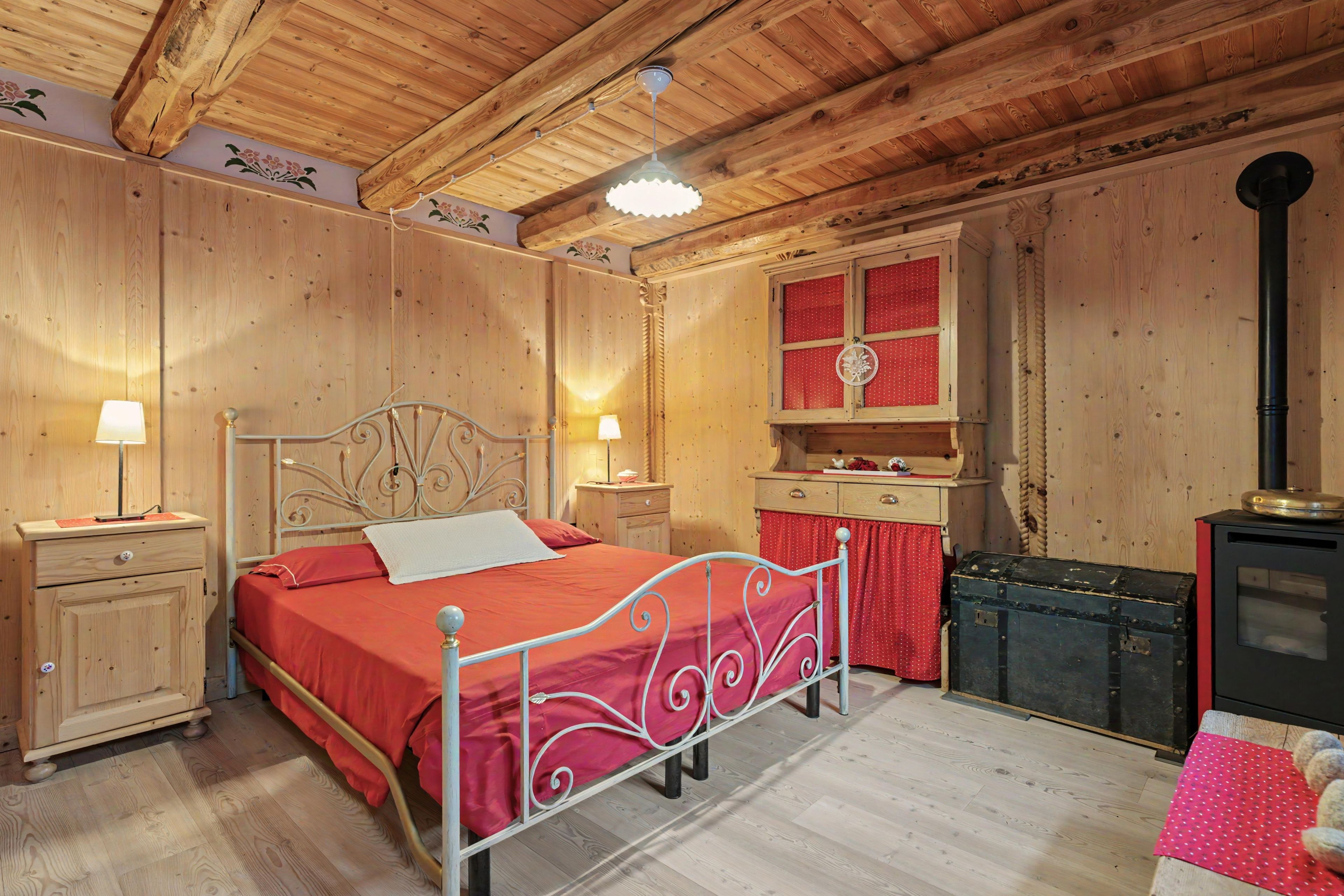 A wooden room with a bed, bedside tables, a dresser, and a stove.