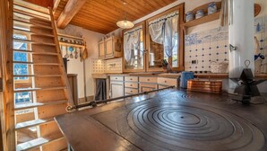 Een keuken met een grote kookplaat, houten kastjes, een hangende rek voor pannen en een houten trap.
