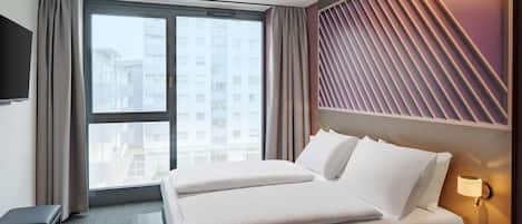A hotel room with a large bed, a desk, a TV, and a window with a city view.
