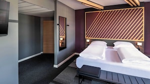 A modern hotel room with a large bed, bedside tables, a flat-screen TV, and a mirror.