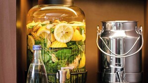 A large glass container filled with lemons and mint leaves, a metal pitcher, and a clear bottle.