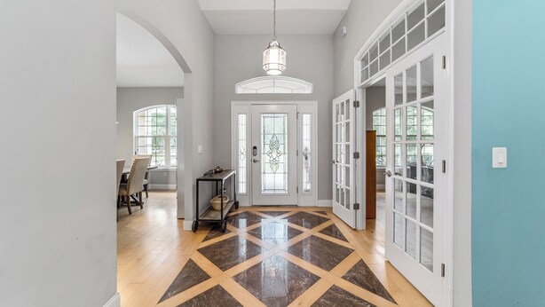 A spacious hallway with a polished floor, a chandelier, and a dining area visible in the background. - Pasture View Estate - 10 min to WEC - Pets Welcome (Ocala)