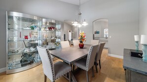A dining area with a glass-fronted display cabinet, a central dining table with chairs, and a chandelier. - Pasture View Estate - 10 min to WEC - Pets Welcome (Ocala)
