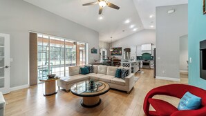 A spacious living room with a large sectional sofa, a glass coffee table, and a red armchair. There is a kitchen in the background with modern appliances. - Pasture View Estate - 10 min to WEC - Pets Welcome (Ocala)
