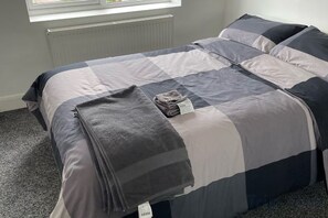 A bed with a grey and white quilt, a folded blanket, and a tag on the bed. - Greenwich Oasis Near o2 arena with Spacious Charm (Greenwich)