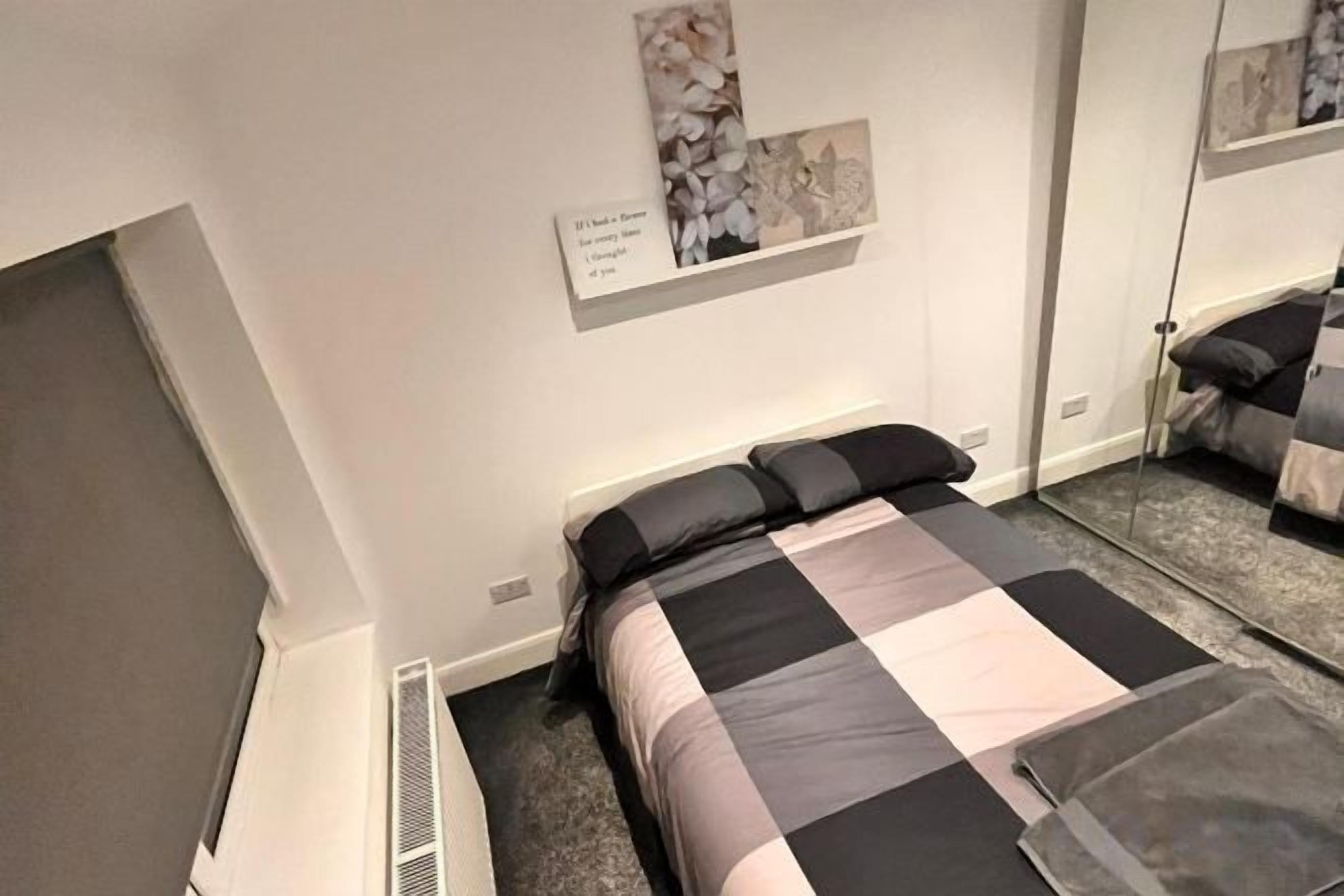 A hotel room with a bed, a bedside table, a mirror, and a wall-mounted artwork.
