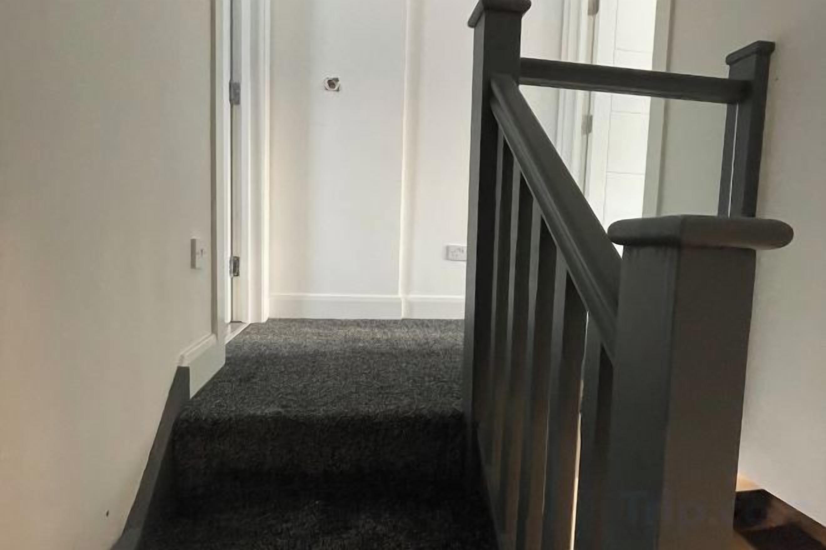 A carpeted staircase with a handrail, leading to a door.