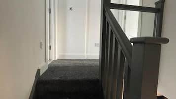 A carpeted staircase with a handrail, leading to a door.