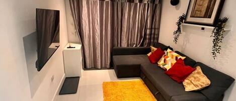 A modern living room with a sofa, a flat-screen TV, a small side table, and a yellow rug.