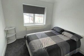 A bedroom with a bed, a window with a blind, a radiator, and a white shelf unit. - Greenwich Oasis Near o2 arena with Spacious Charm (Greenwich)