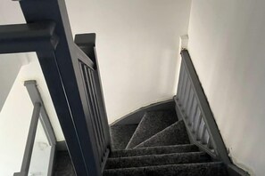 En trappe med mørkt tæppe og gelænder, der fører op til en platform med en hvid væg.