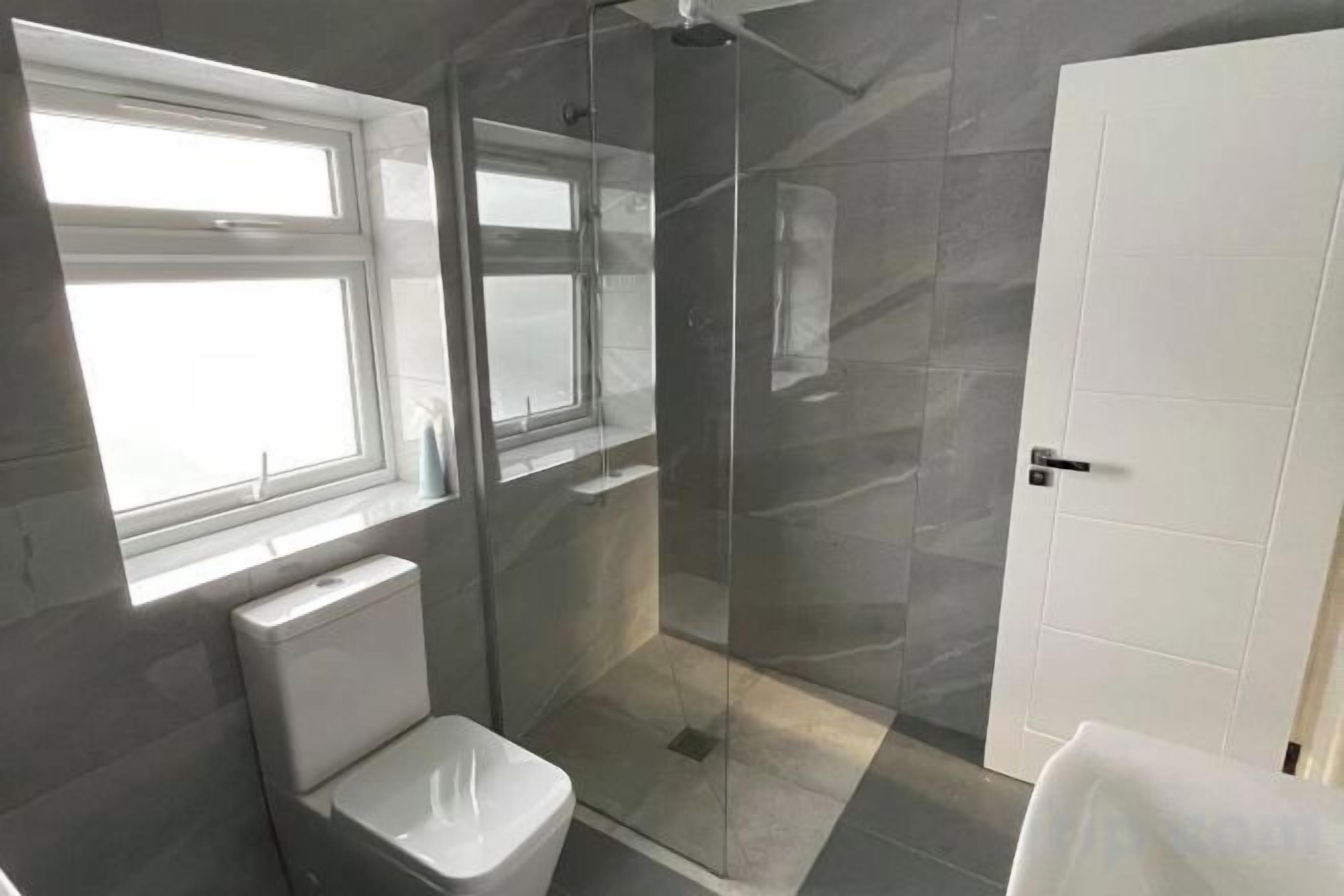 Een badkamer met toilet, een douchecabine van glas en een witte deur.