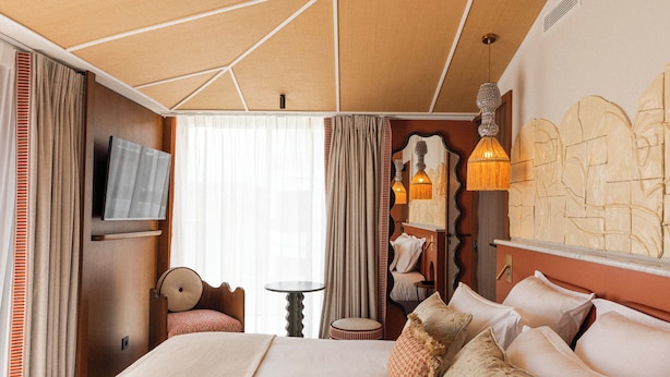 Una camera d'albergo con un letto, tende, una televisione, un tavolo e una lampada fissata al muro.