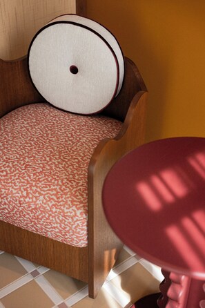 A wooden chair with a patterned cushion, a round table, and a tiled floor.