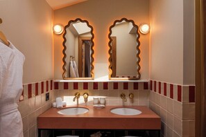 A bathroom with two sinks, a towel rack, and a mirror with a unique wavy frame.